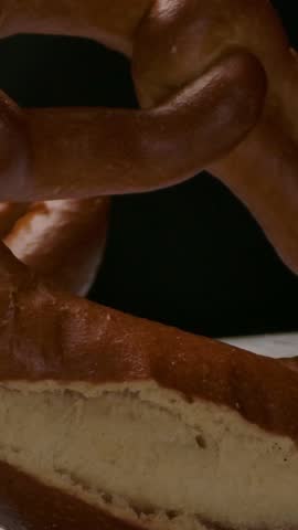 Camera zooming in to freshly baked pretzels tilting back while being arranged on timber table in dark room. Vertical shot.