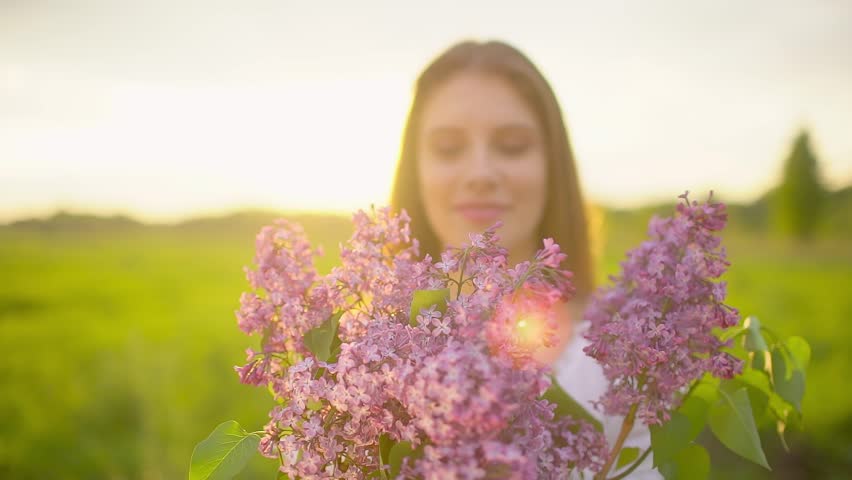 Happy beautiful woman smelling blooming flowers lilacs at nature meadow sunset. Young teenage girl touching hands in summer park. Beauty, happiness, aroma, perfume, fragrance, spring, travel, relax
