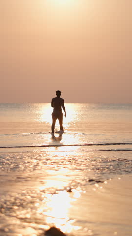 Young man walking towards the rising sun reflected in the shallow waters of a tropical beach