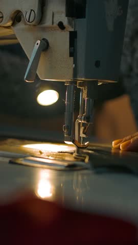 Working sewing machine presser foot, stitching in slow motion. Tailor's hand holding sewing leather carefully. Manufacturing individual leather bags, belts, accessories. Vertical shot.