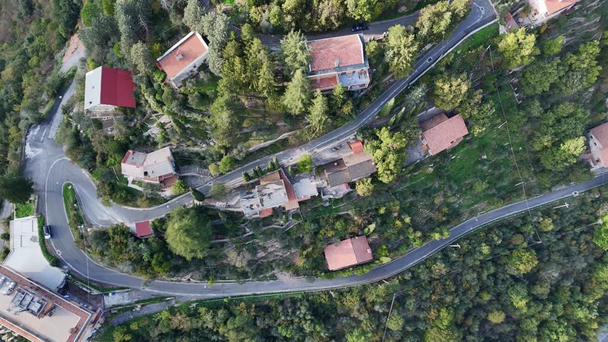 Serene village nestled in green hills showcases winding roads and charming homes under a clear blue sky