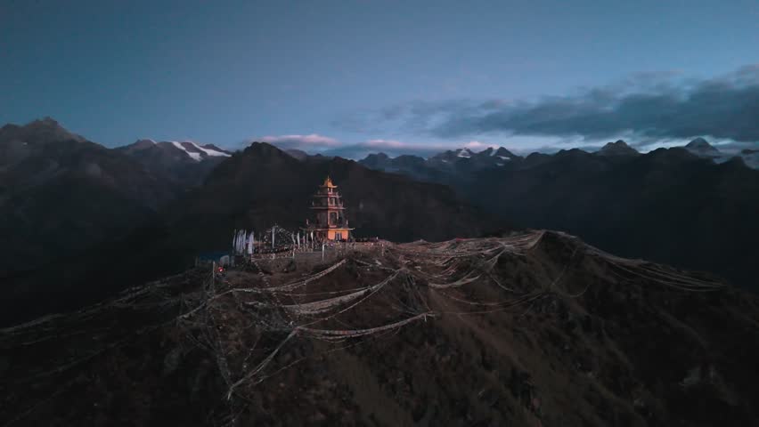 A mountaintop Buddhist stupa surrounded by vibrant prayer flags, set against a dramatic Himalayan backdrop under a clear blue sky.