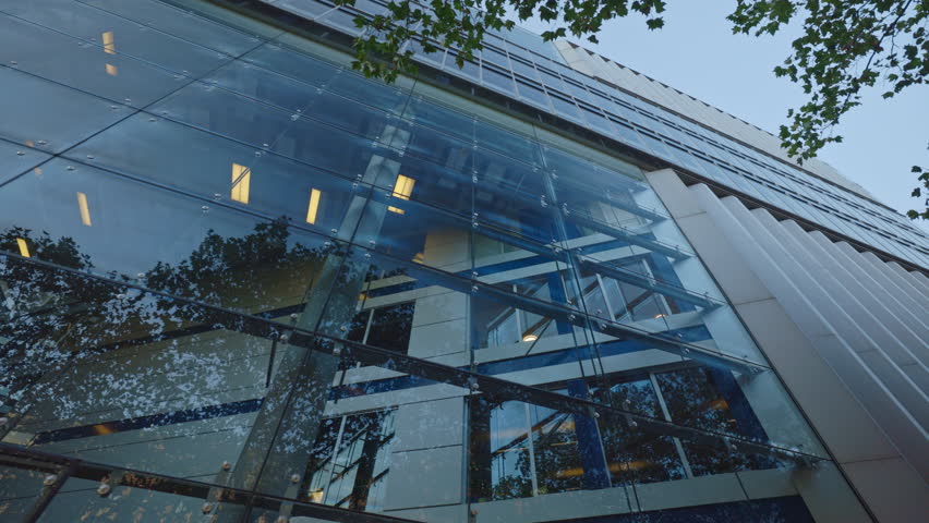 Glass wall and shutters on facade of modern business center on street low angle shot. Stylish office building ideal for bank and company headquarter in downtown block at twilight