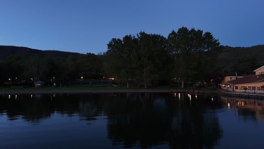 Twilight reflections over a serene lake surrounded by lush greenery and distant hills at dusk