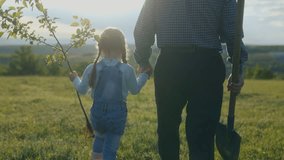 Senior man and young girl seen from behind, walking across a grassy field on a sunny morning, holding a shovel and a sapling, ready to plant a new tree together. - Powered by Shutterstock - Get 15% off with code: PIKWIZARD15
