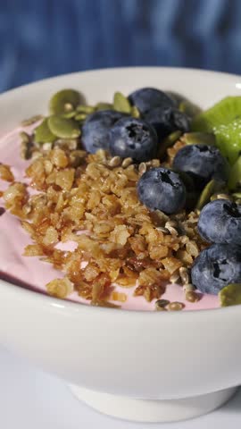 white breakfast bowl with jogurt and fruits turning on  blue background, food closeup, healthy eating