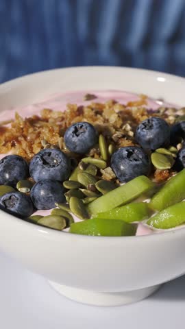 white breakfast bowl with jogurt and fruits turning on  blue background, food closeup, healthy eating