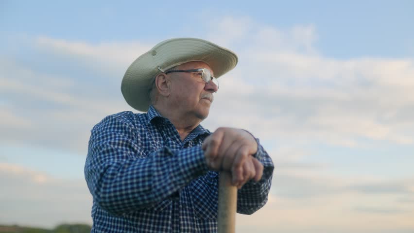 Aged American farmer leans on his stick at sunset, alone in the field. A deep portrait of a man connected to earth, time, and his unspoken story.