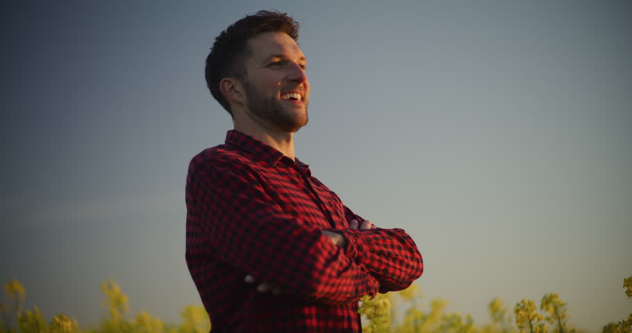 Portrait of a happy and proud farmer standing in a beautifully blooming yellow rapeseed field.