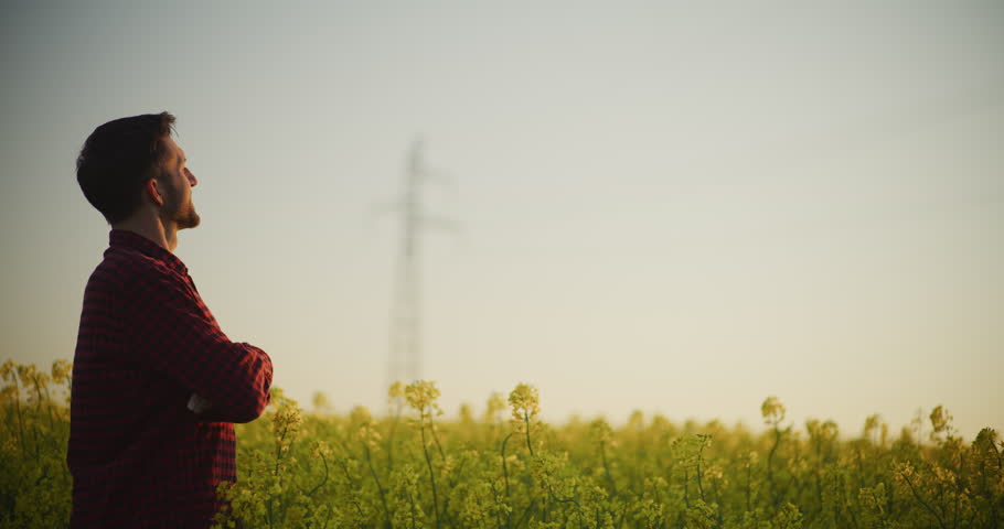 A content farmer stands proudly in a beautifully blooming rapeseed field, symbolizing satisfaction and agricultural success.