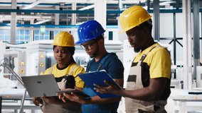 All black inspectors team in photovoltaics factory look over documents, review performance of robot arms placing solar panels on assembly lines. Supervisors inspecting solar cells plant. Camera A. - Powered by Shutterstock - Get 15% off with code: PIKWIZARD15