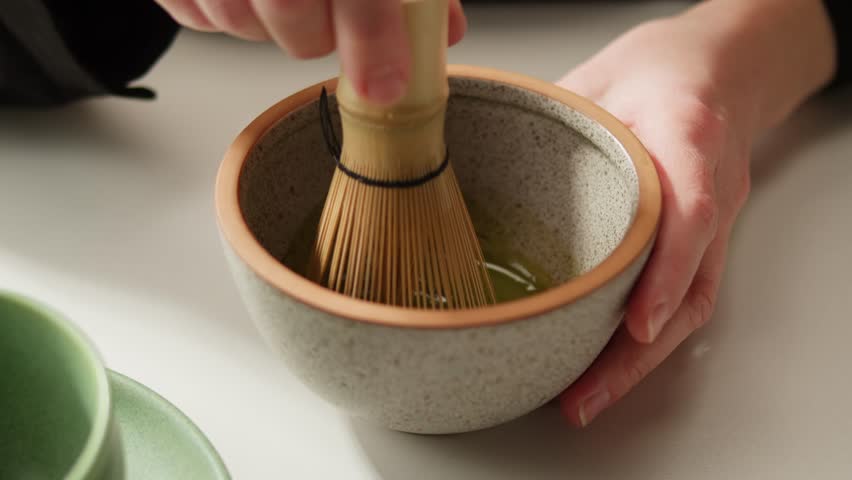 Matcha green tea cooking process, japanese powder green tea in a bowl with bamboo whisk, macro close up in cafe of powder green tea. 