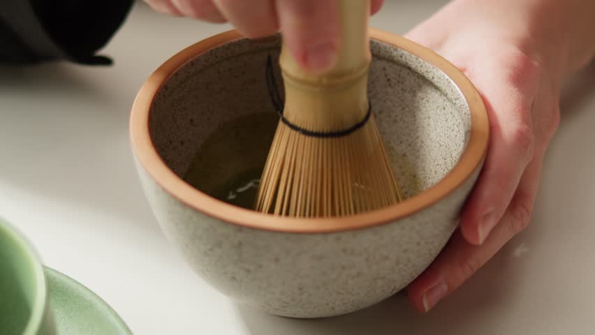 Matcha green tea cooking process, japanese powder green tea in a bowl with bamboo whisk, macro close up in cafe of powder green tea. 