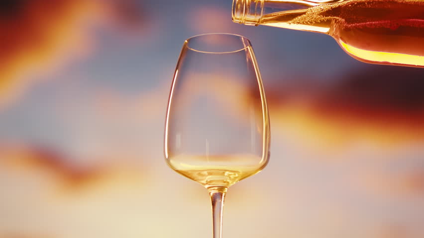 Orange or white rose wine bottle and glass against a sunset in a peaceful vineyard, pouring of ecological natural wine in hotel or sunset bar restaurant, cheers friends.
