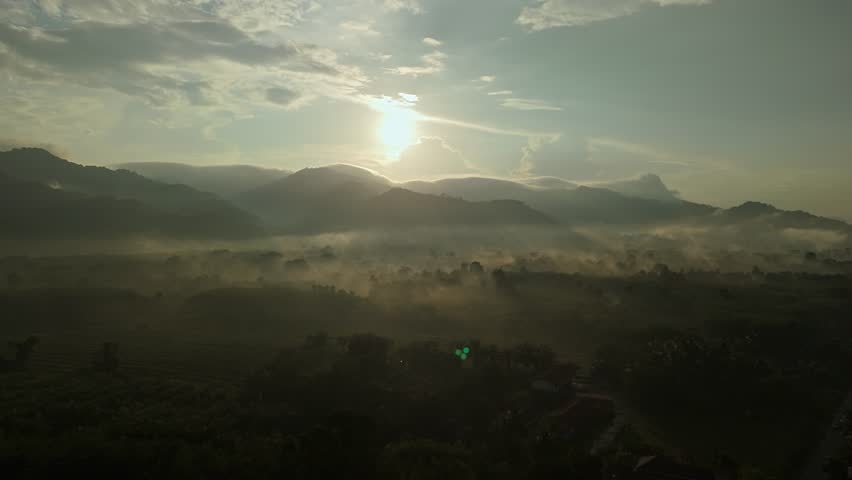 Aerial view of sunrise over mountainous landscape, with thick fog blanketing. Sun