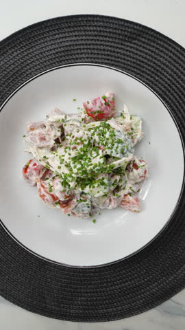 Vertical footage Professional chef's hands preparing summer salad with crisp lettuce, ripe tomato, cucumber, drizzling chive cream sauce on pristine white plate