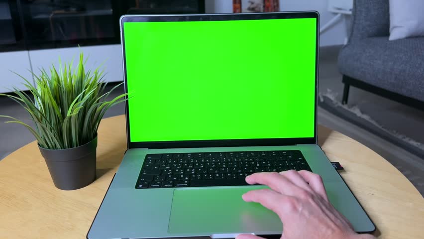 4K shot of a hand interacting with a laptop featuring a green screen, ideal for UI mockups, branding inserts, tech presentations, or software promo overlays. Clean background and modern setup.