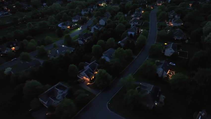 Glowing houses and homes in quiet american neighborhood. Aerial top down flyover. Large Single family houses at night. Villas and apartments in suburbia.
