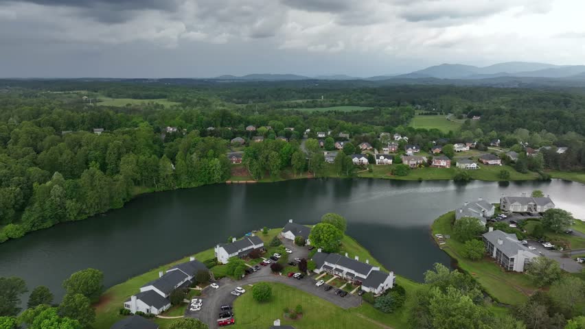 Aerial panorama modern townhouses and homes at lake in Virginia. Dark Cloudy day in forest landscape. Quiet and green scenery of United States.