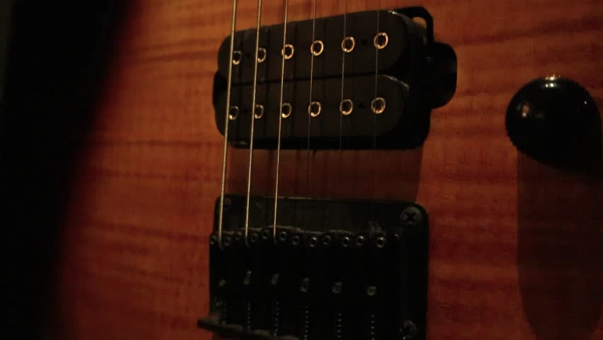 Cluse up view of an electric guitar. Detail of instrument along guitar wooden pickguard, fingerboard and golden strings to guitar neck. illuminated guitar in dark room highlighting the fine details