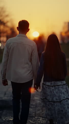 Loving couple holding hands, walking together on tree-lined path during golden sunset, sharing tender moment in warm evening glow
