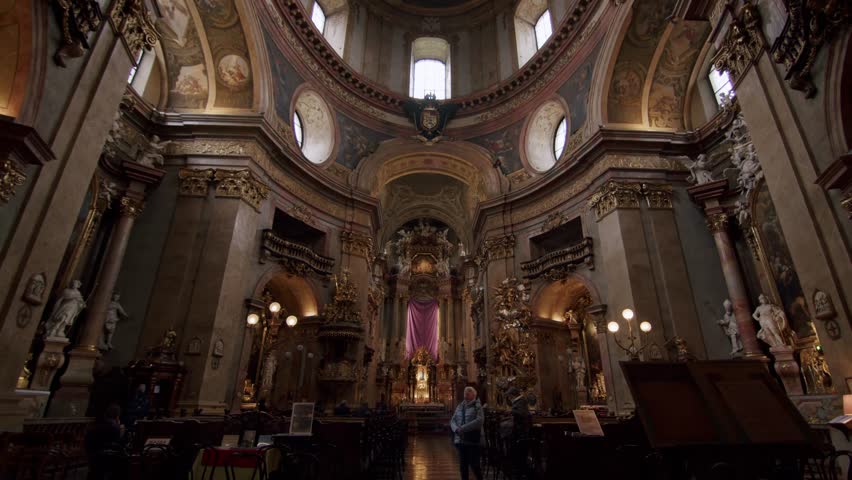 Vienna , Austria - 05 30 2024: Golden-lit baroque church interior with tourists, full view of Vienna