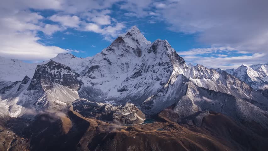 Majestic Ama Dablam peak time-lapse in the Himalayas, Nepal. Dynamic clouds drift across a blue sky over rocky slopes and a small lake. Dramatic mountain landscape.