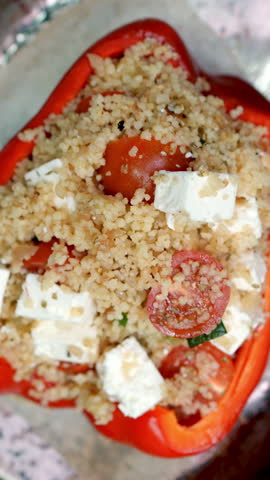 Vertical footage Professional chef stuffing red bell pepper with couscous, feta, cherry tomatoes, then placing seasoned pepper on metal tray for roasting in hot oven