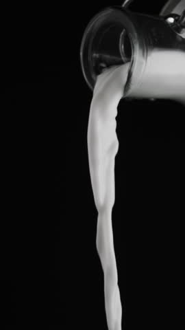 Pouring milk from a bottle of milk into the glass on black background. Vertical slow motion footage.