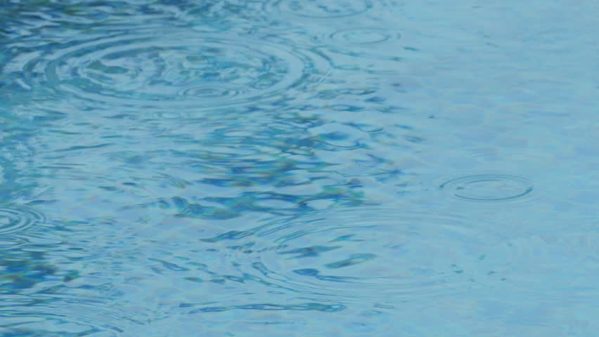 Raindrops falling on the smooth surface of the pool. Slow motion Mid shot view.