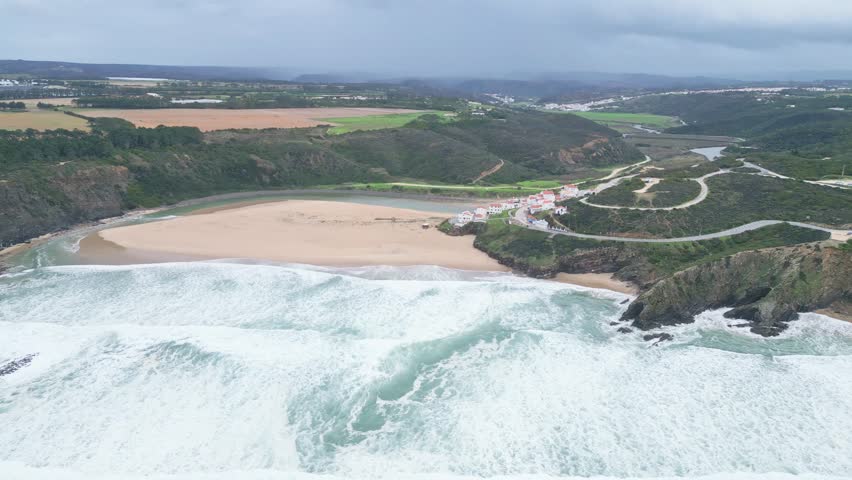 Sweeping beach with waves, cliffside village and lush hills in Aljezur, Portugal