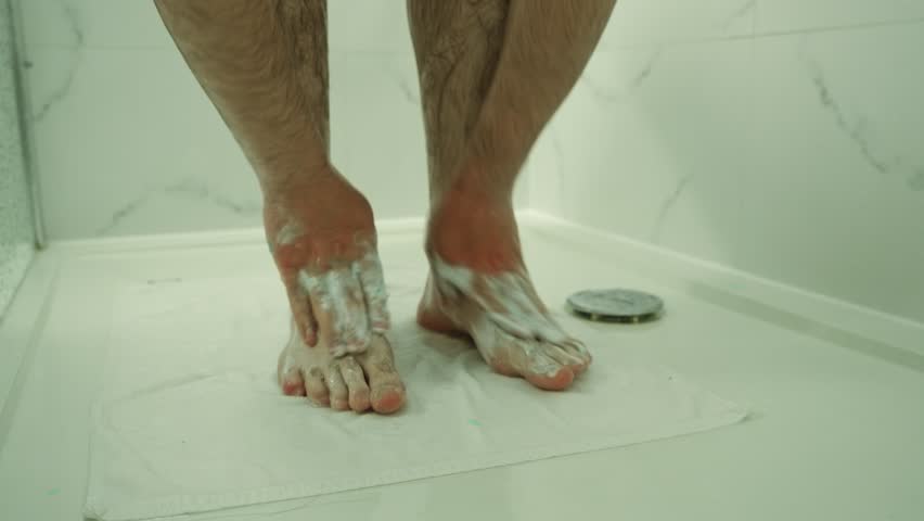Man washing hairy legs in shower. Cleaning feet with soap in tiled bathroom. Rubbing lather on lower legs during hygiene routine. Morning shower focusing on personal care and cleanliness
