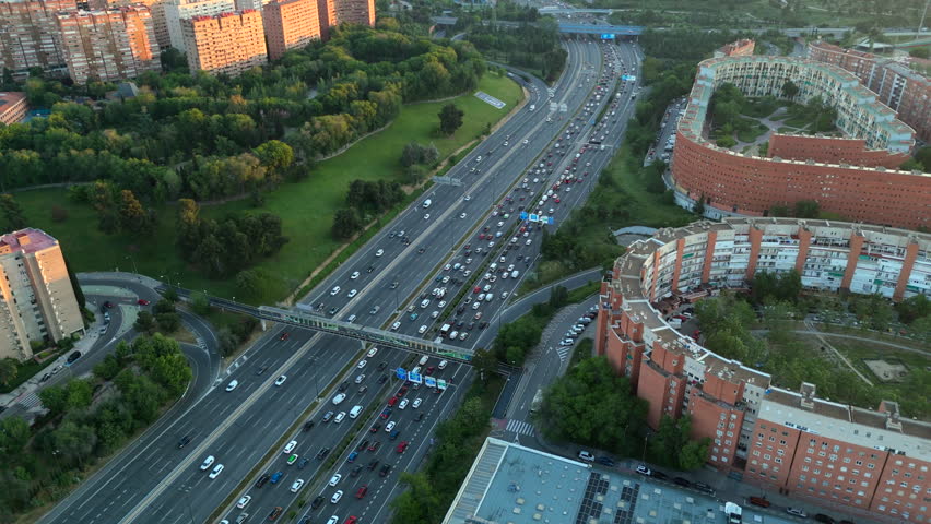 Top-down aerial shot of Madrid’s M-30 highway during sunset, showing heavy traffic, residential blocks and green areas. Ideal for themes of mobility, congestion and city infrastructure