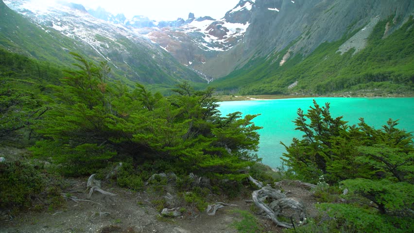 Esmeralda Lake, Ushuaia, Tierra del Fuego, Argentina. Turquoise lake water surrounded by green forest, valley walls, and distant snow-capped mountains in Patagonia.