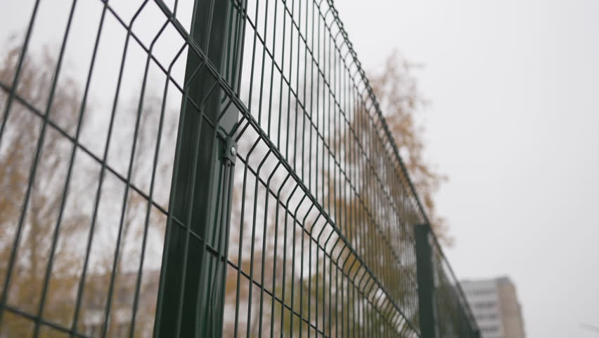 Wired fence shows structured pattern near football field closeup. Sharp metal lines frame view of empty sports zone during cold season