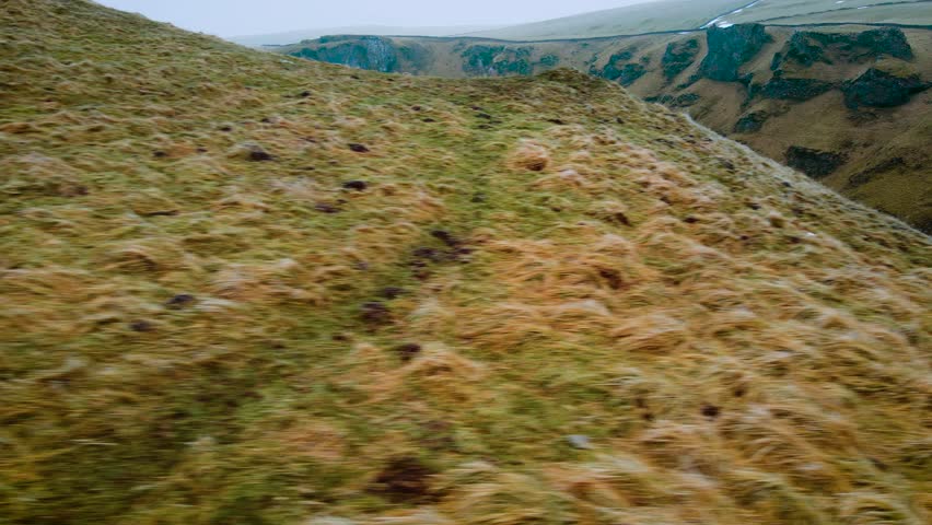 Car traveling through steep mountain valley with grassy slopes. White vehicle moving along winding route in Peak District, United Kingdom. Aerial view of curving road cutting through rugged hillside