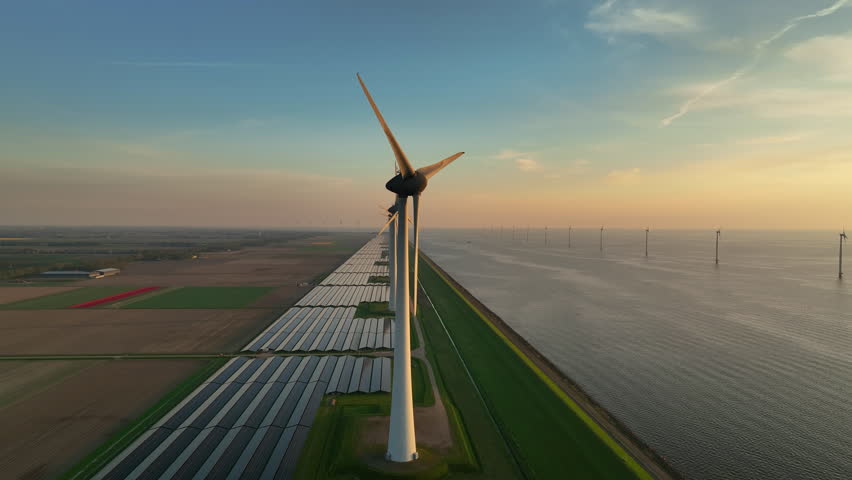 Wind turbines and solar panels on a lakeshore producing sustainable energy during springtime sunset seen from above.