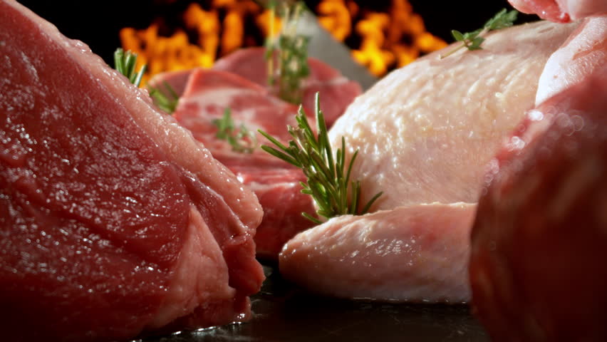 Slow motion, camera move. Large assortment of premium raw meat, beef, sausages, pork and chicken suitable for butchery advertising, fire on background