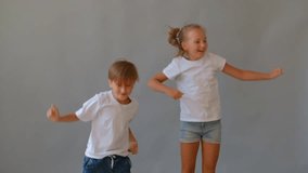 Two joyful fair-haired children, a boy and a girl, jumping and dancing with arms raised against a plain grey background. Suggests excitement, energy, and a playful mood between siblings or friends - Powered by Shutterstock - Get 15% off with code: PIKWIZARD15