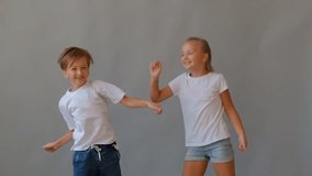 Two joyful fair-haired children, a boy and a girl, jumping and dancing with arms raised against a plain grey background. Suggests excitement, energy, and a playful mood between siblings or friends - Powered by Shutterstock - Get 15% off with code: PIKWIZARD15