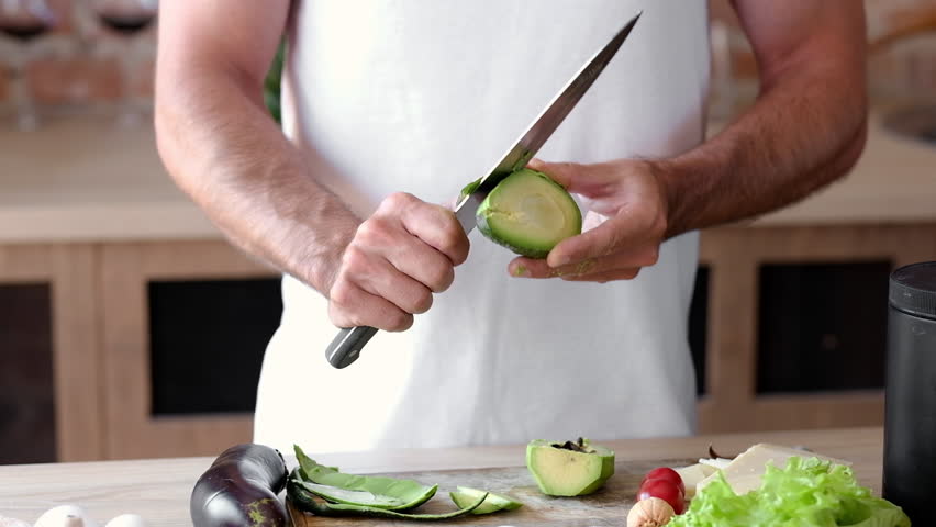 Young Man Peeling Ripe Avocado In The Kitchen, Preparing Healthy Vegetarian Breakfast Ingredients