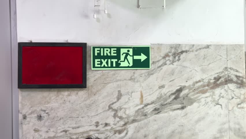 static shot of Fire Exit Sign and a notice board placed on the wall to guide people in case of emergency