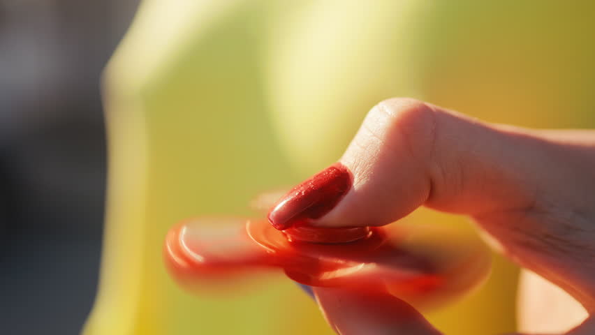 A CloseUp of a Hand Actively Spinning a Bright Red Fidget Spinner Against a Colorful and Bright Background
