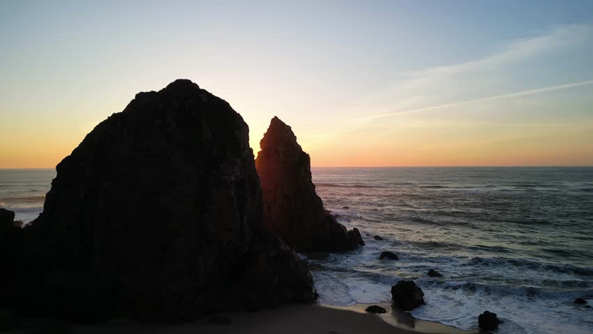 Witness the stunning sunset illuminating the rocky seashore and waves crashing against cliffs