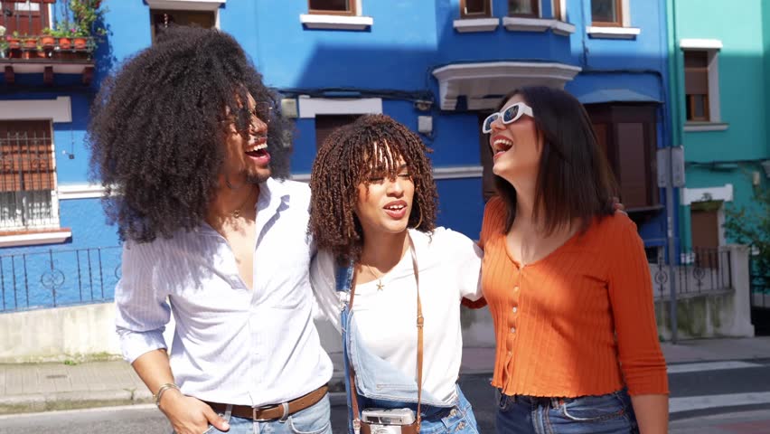 Joyful young tourists bonding and creating memories while posing near vibrant blue urban building during sunny summer holiday