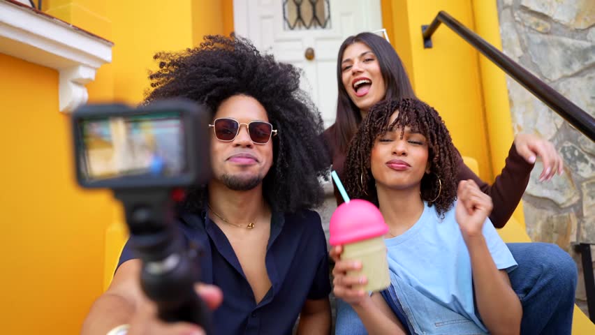 Young influencers recording vlog, sipping milkshake on vibrant yellow doorstep during summer leisure moment