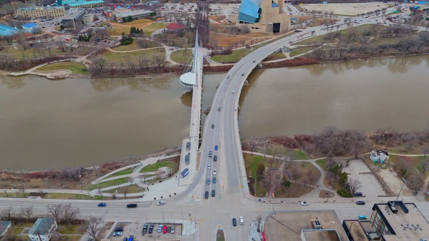 Sweeping aerial shot of the Canadian Museum for Human Rights, Esplanade Riel bridge, and the full downtown Winnipeg skyline under glowing sunset skies.