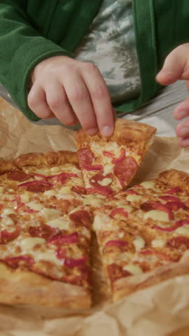 Vertical close-up tilt-up shot of hungry man enjoying delicious pepperoni pizza, sitting on couch in living room