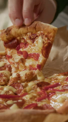 Vertical close-up shot of unrecognizable man taking delicious cheesy pepperoni pizza slice