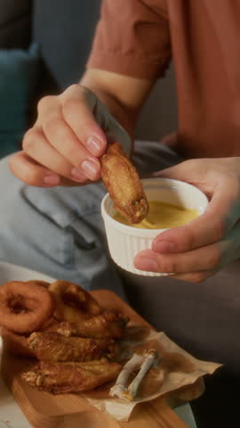 Vertical close-up shot of unrecognizable man dipping fried fast food snacks in cheese dipping sauce